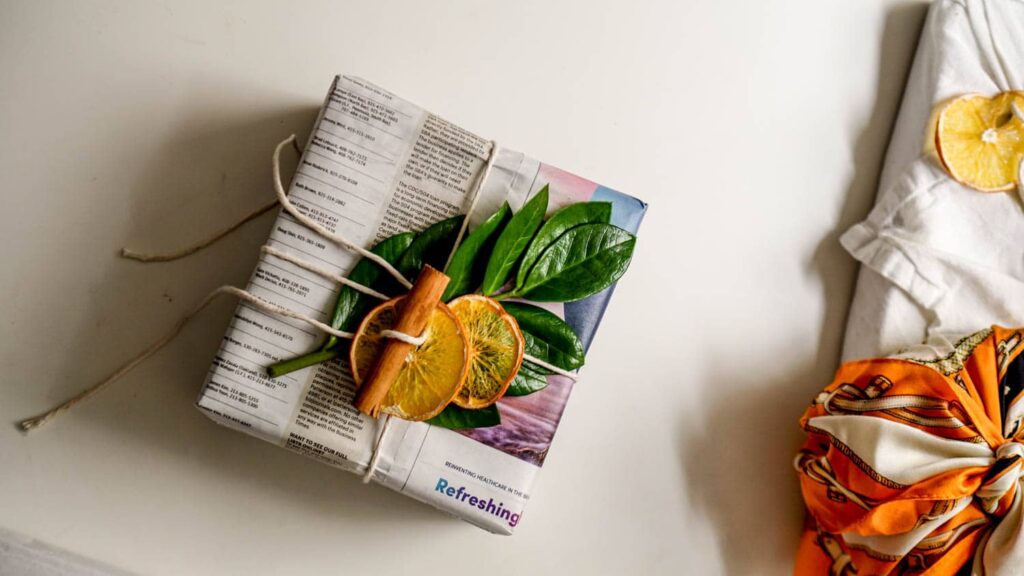 A gift wrapped in newsprint and adorned with dried orange slices, cinnamon, and greenery to showcase sustainable gift wrapping ideas