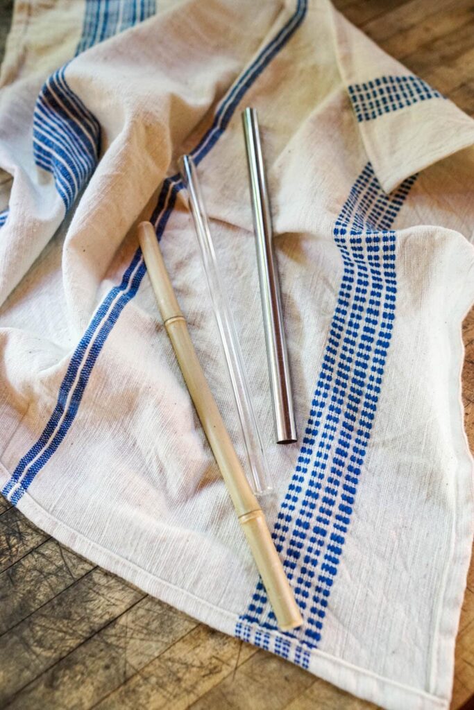 overhead image of three reusable straws (made from bamboo, glass, and stainless steel) on top of a reusable cloth rag