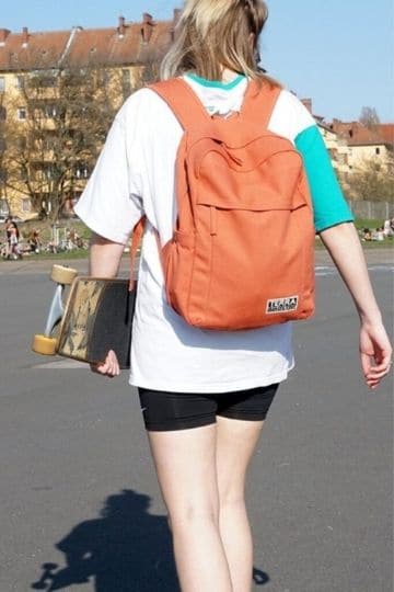 someone walking with sustainable backpack holding a skate board