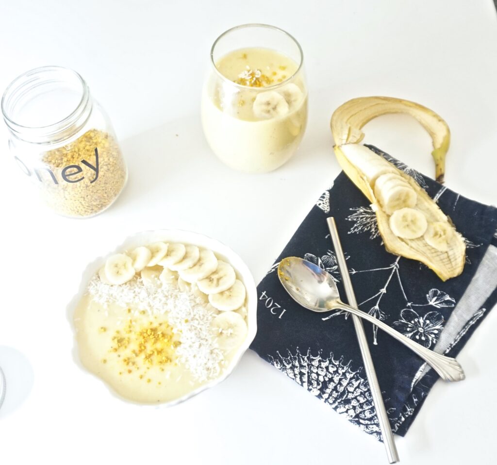 Pineapple mango smoothie recipe served in a bowl and topped with bee pollen, coconut shreds and banana slices.