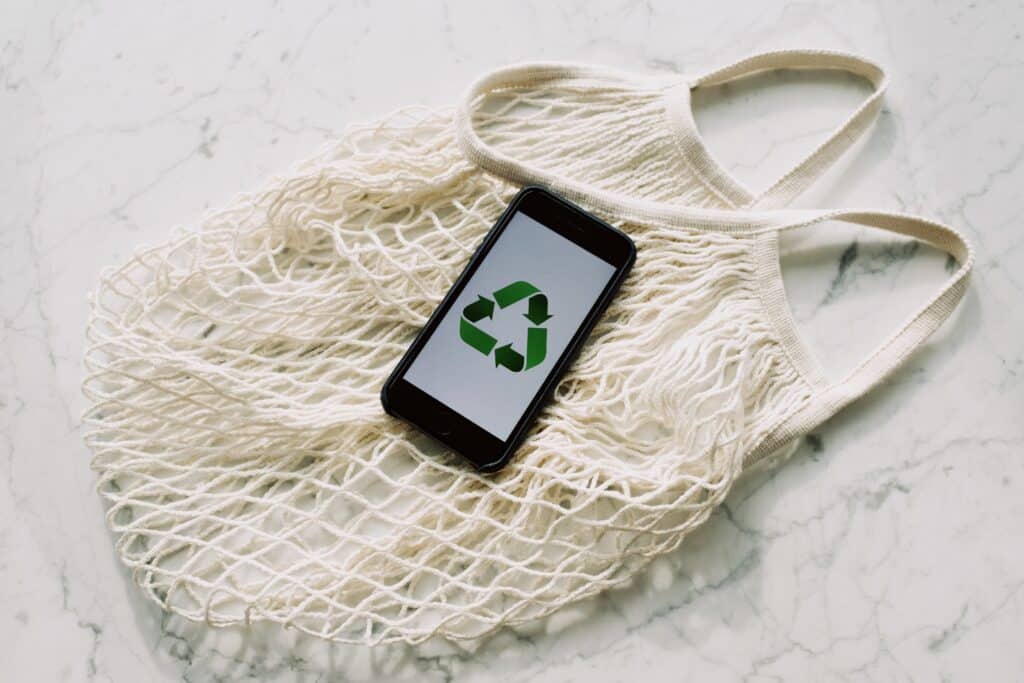 a reusable bag and a phone with the recycle symbol on the screen showing ways to live zero waste