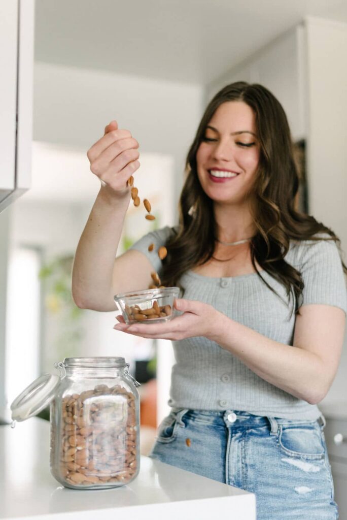 A woman dropping a handful of almonds into a bowl for these almond recipes
