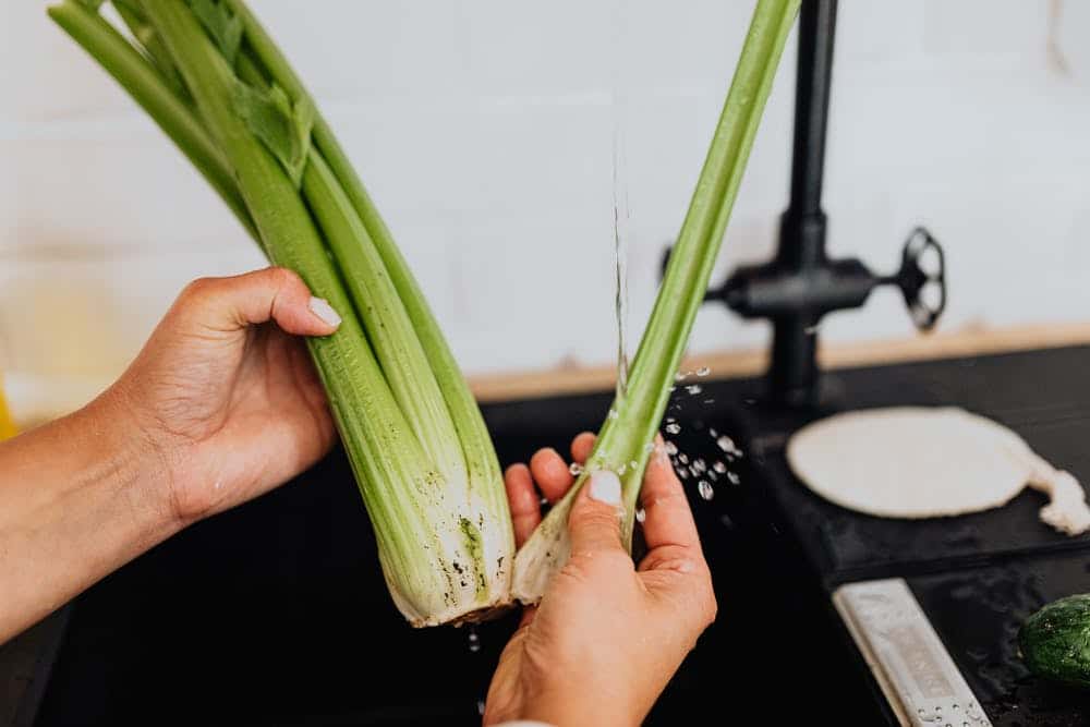 celery greens being hand washed in a sink