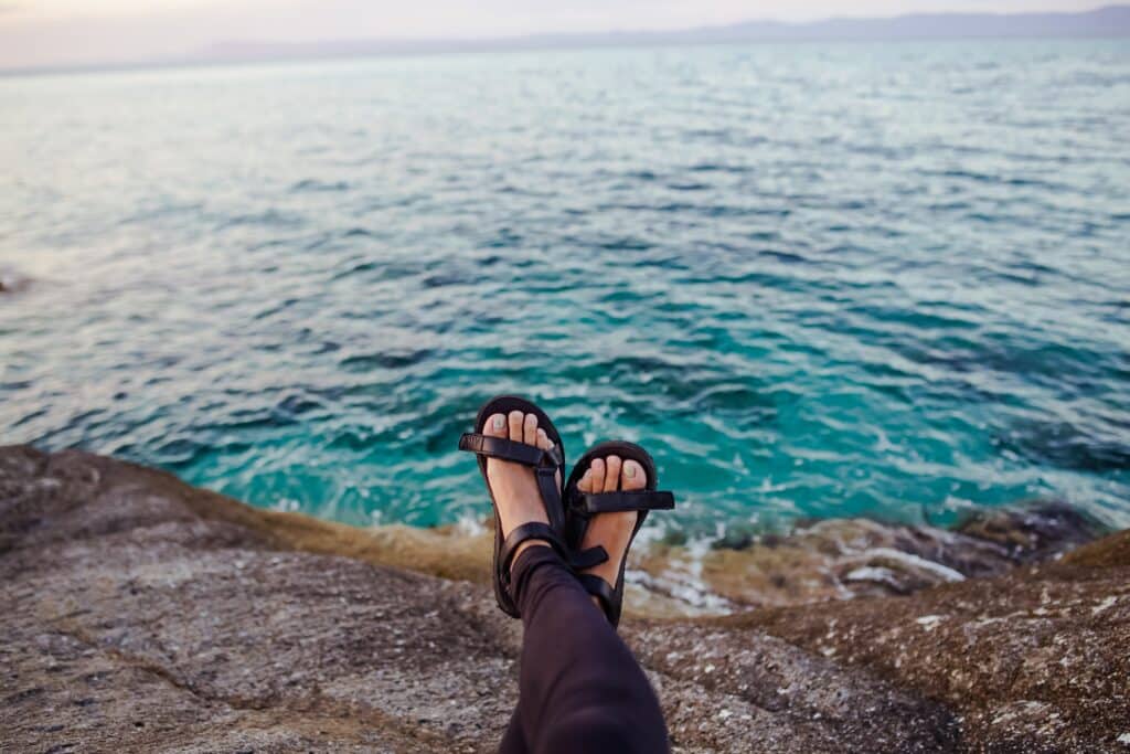 Photo of feet wearing eco shoes, sitting on the rocks near the ocean.