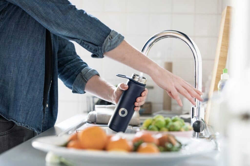 Hands refilling a metal recycled water bottle out of the sink. 