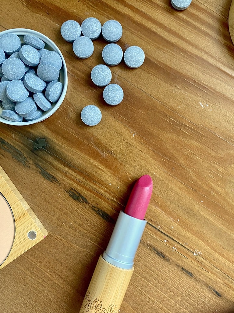 a sustainable bathroom includes sustainable make up - a pink lipstick on a wood table.