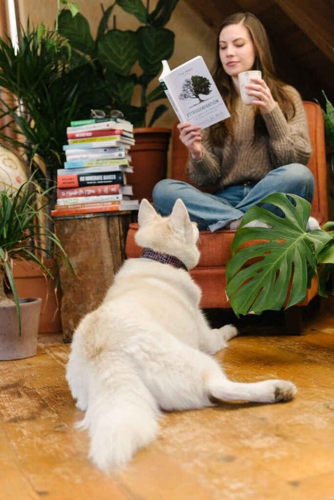 Woman reading next to a stack of sustainable living books with a dog at her feet.