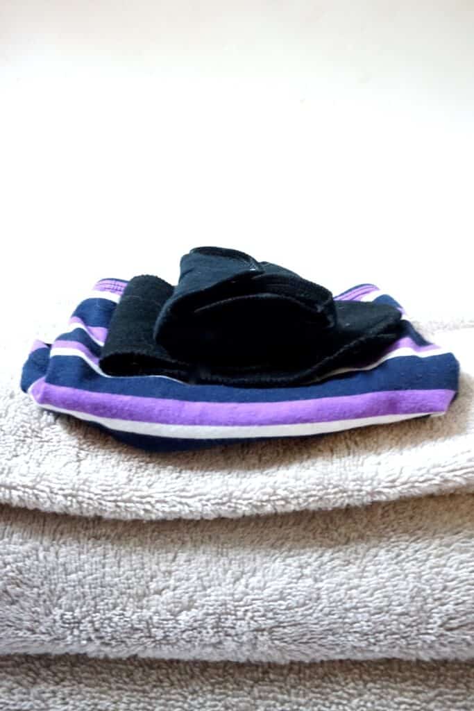 Close up of reusable pads for periods and period panties on top of a stack of towels. 