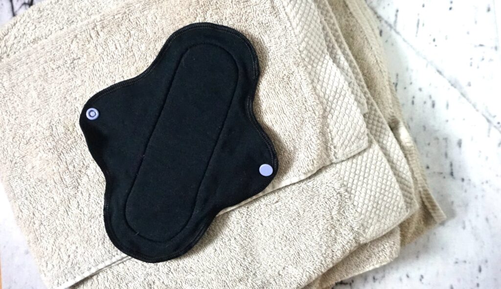 An open cloth pad for period on top of a stack of towels.