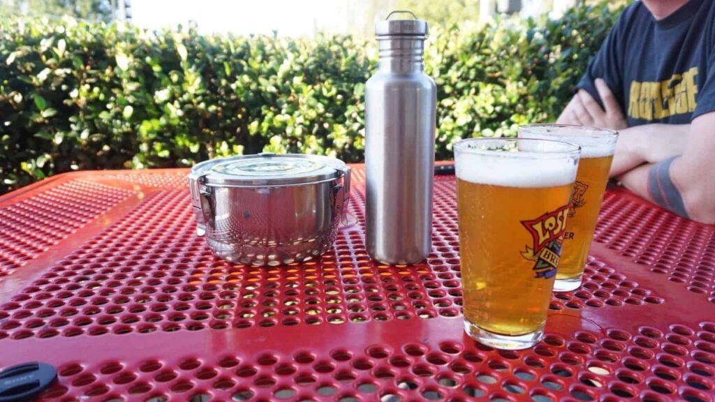 A tiffin, Kleen Kanteen, and two glasses of beer on a picnic table.