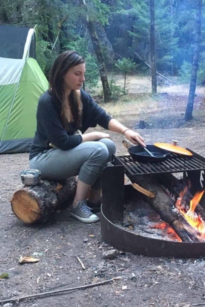 A woman cooking over an open fire during a sustainable camping trip.