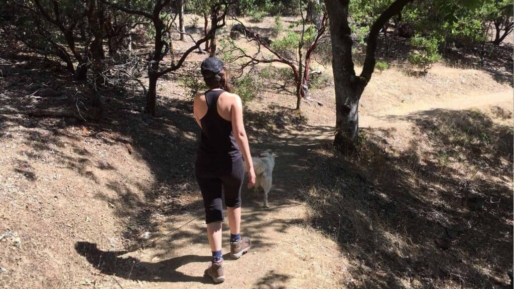 A woman on a hiking trail with her dog on a zero waste camping trip.