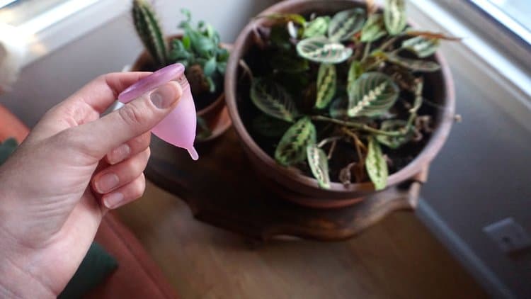 a woman's hand holding a period cup, one of the featured zero waste period products.