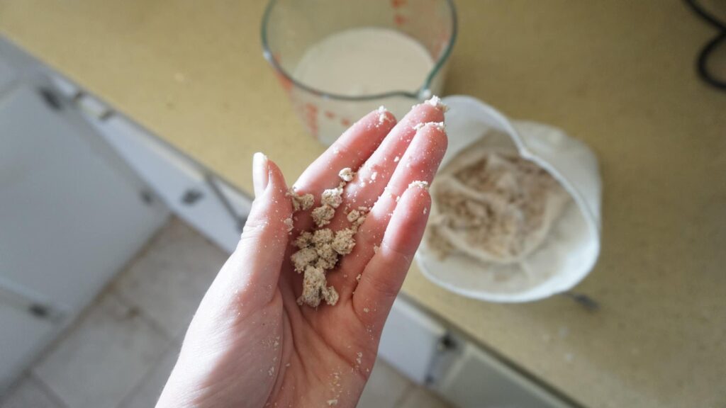 Nut milk bag vs. cheesecloth: a photo of a hand holding almond pulp with a nut bag in the background.