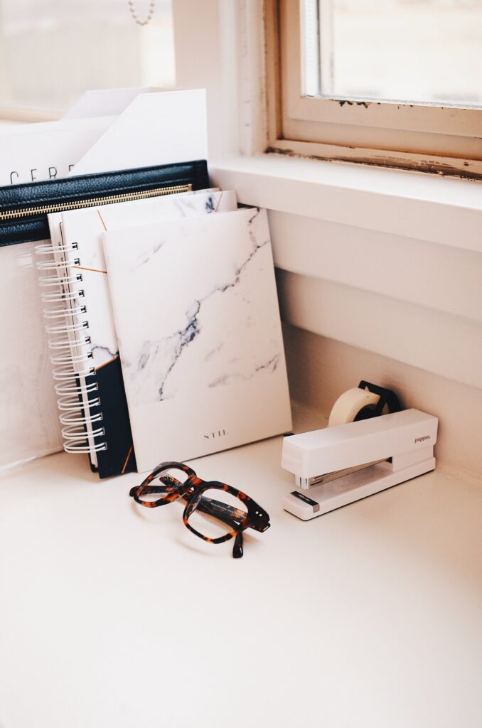 a desk full of notebooks, tape, a stapler, and reading glasses - potential tools of a sustainability team. 