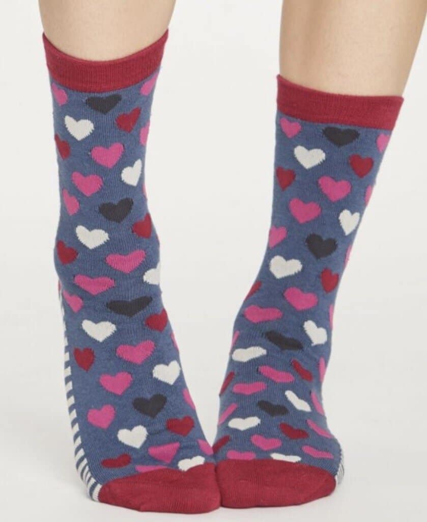 Woman's feet wearing blue socks with pink, white, and gray hearts on them. 