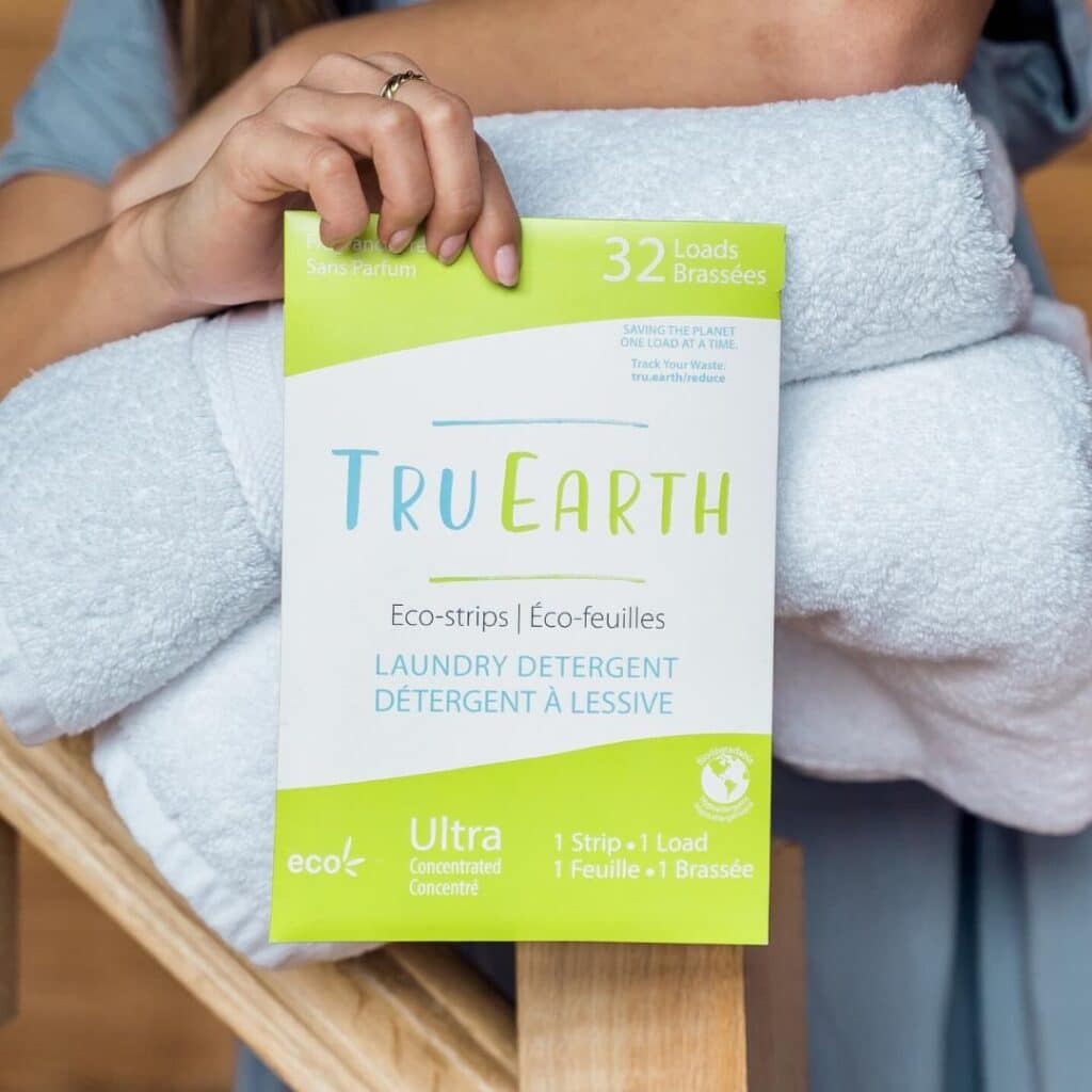 Woman's hand holding a package of Tru Earth in front of as tack of folded towels. 