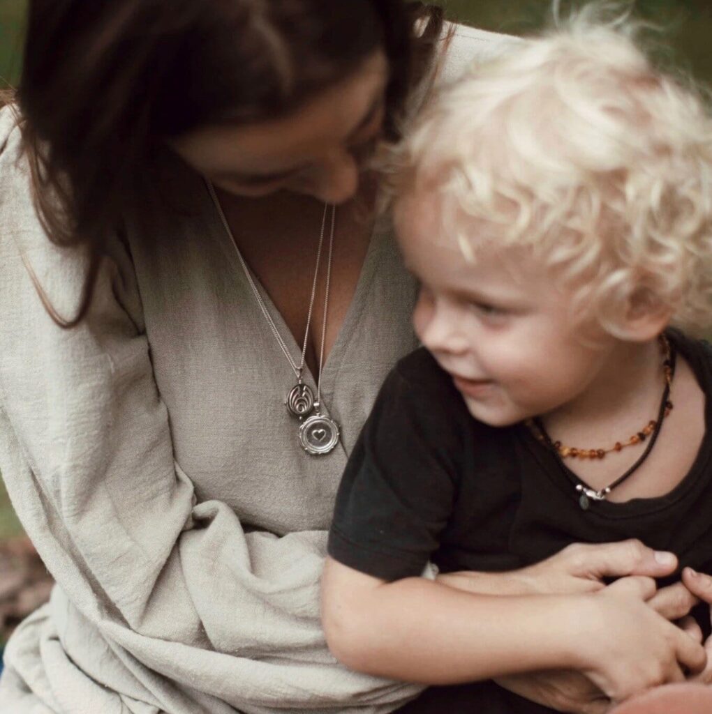 Woman wearing 2 silver pendants and hugging a child.