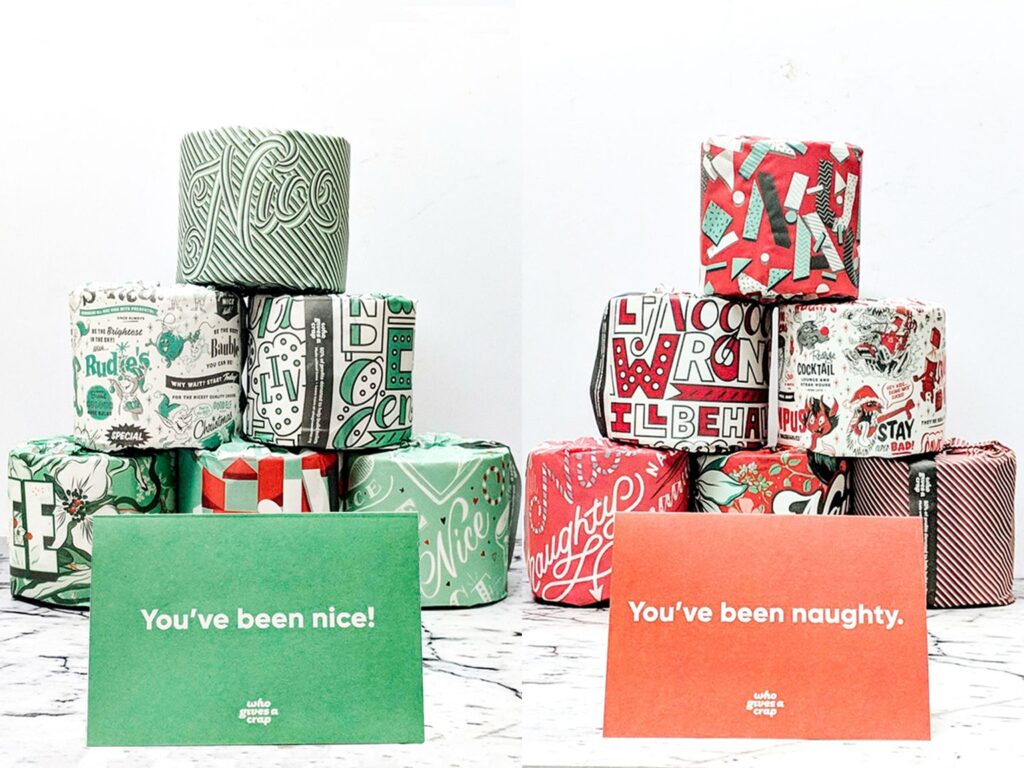 Two stacks of Who Gives a Crap toilet paper, one packaged in green with a card that says "You've been nice!" and one packaged in red that says "You've been naughty."