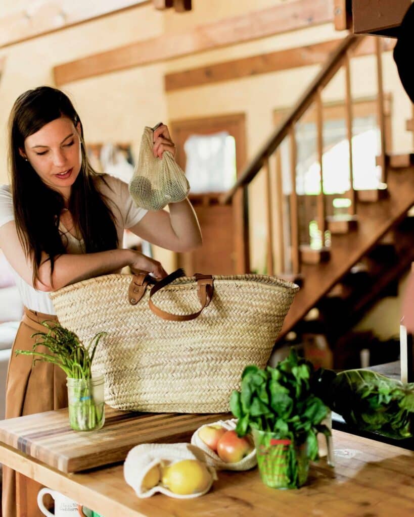 Woman placing produce bagged in reusable bags into her tote instead of grocery bags for a  post about easy eco friendly swaps. 