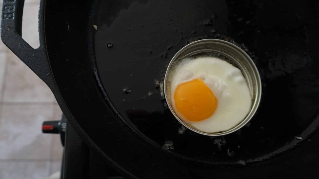 The lid from a mason jar with lid used as an egg ring in a cast iron skillet