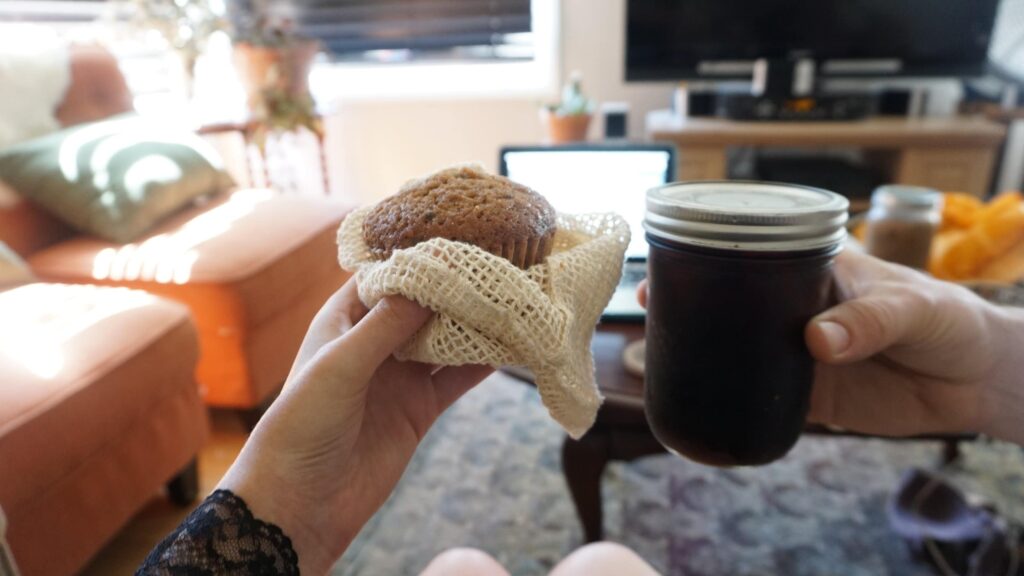 Hands holding a breakfast muffin and their morning coffee, using mason jars as drinking glasses