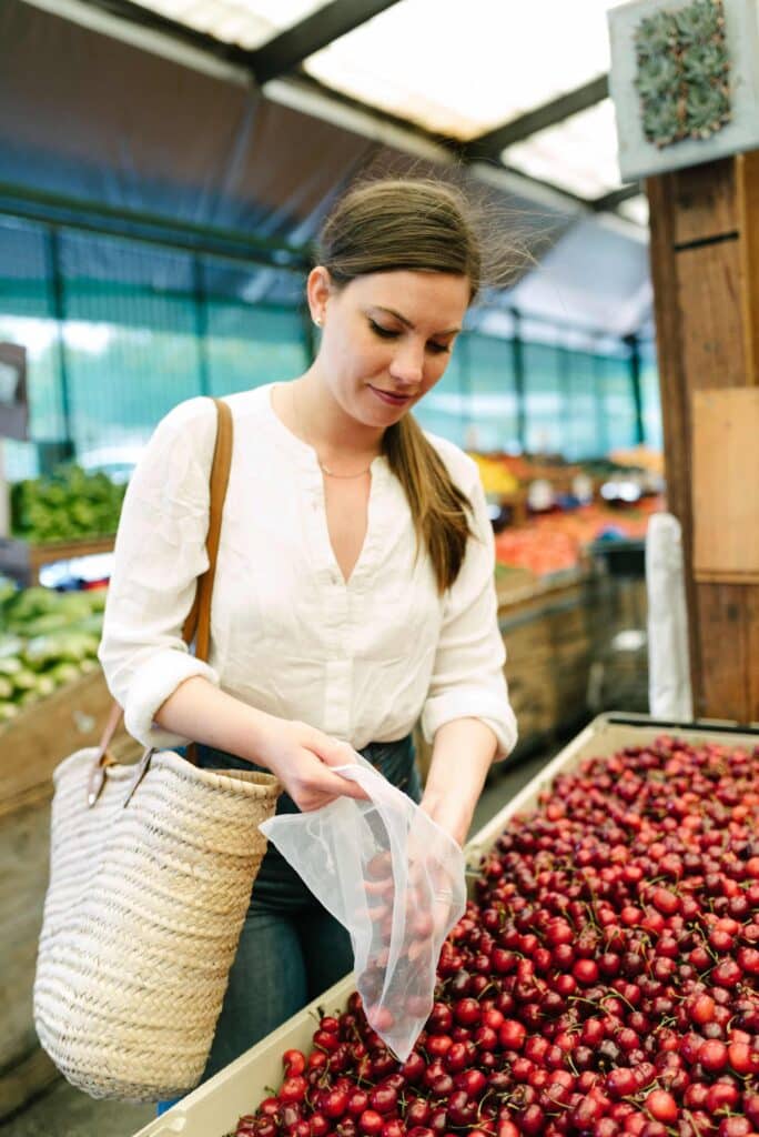 Woman placing fresh cherries into a reusable produce bag, one of the suggested sustainable swaps in this post. 