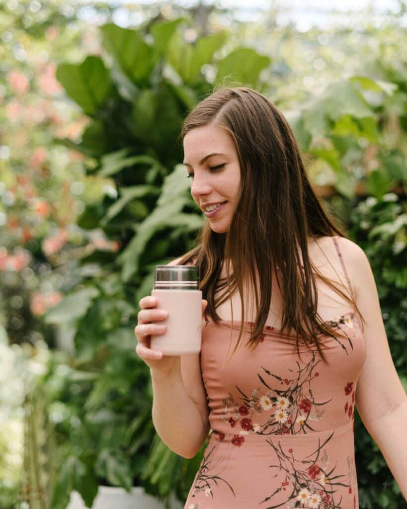 Woman drinking from a pink thermos, a cute and easy zero waste swap to disposable cups. 