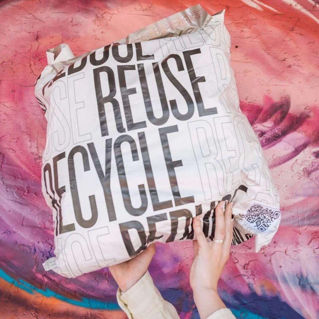 Plastic bag with the words "reduce, reuse, recycle" on it that's full of clothes recycling