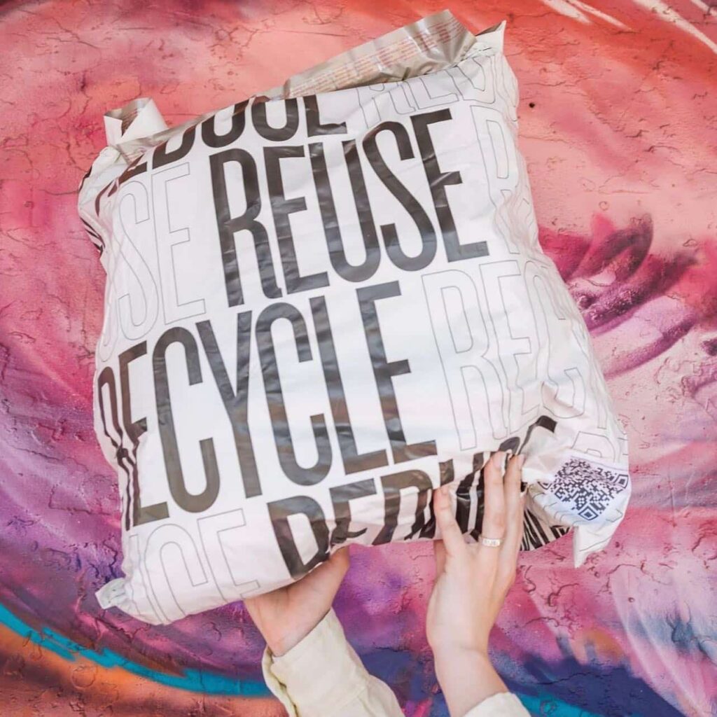 Plastic bag with the words "reduce, reuse, recycle" on it that's full of clothes recycling 