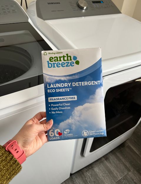 Photo of Earth Breeze laundry sheets held in front of a washer and dryer. 