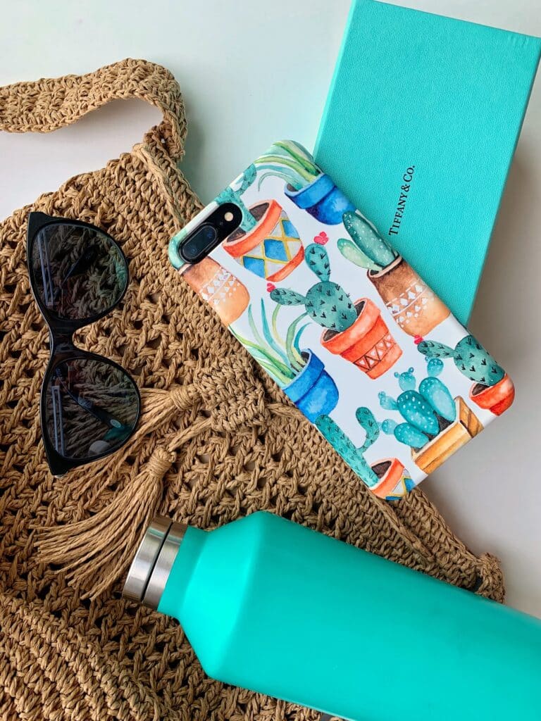 a phone in a biodegradable phone case with a tote, sunglasses, Tiffany & Co box and teal water bottle.