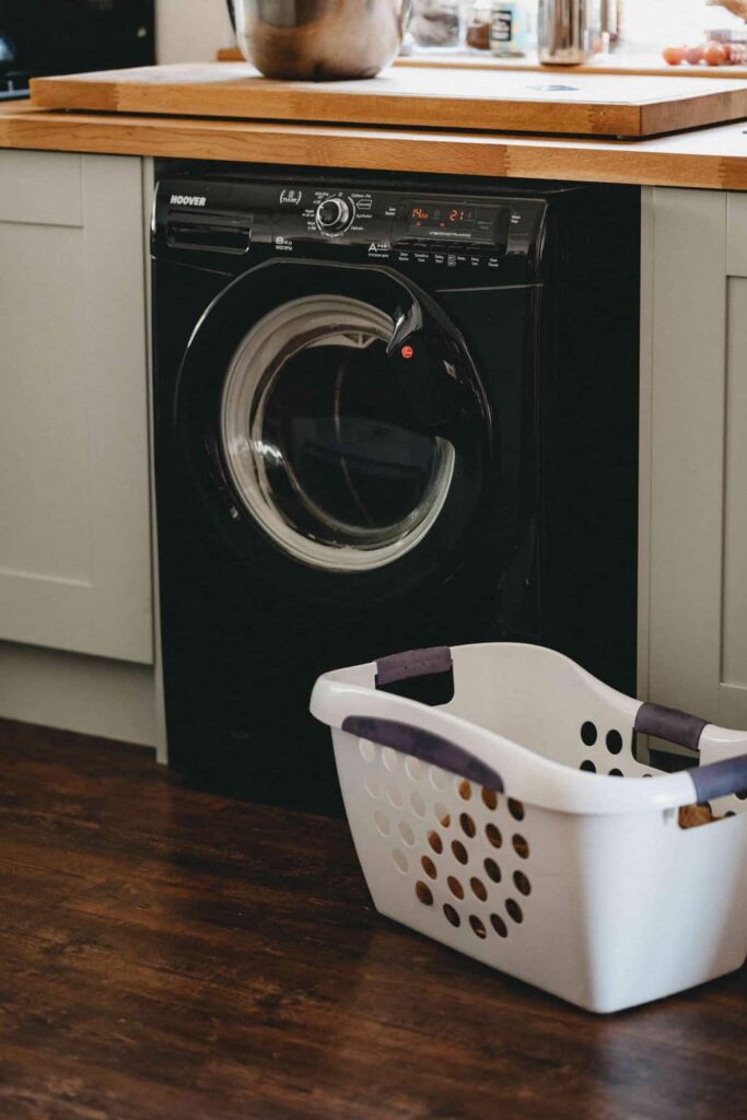 A washing machine with an empty laundry basket next to it in a post about why you shouldn't use homemade laundry soap 