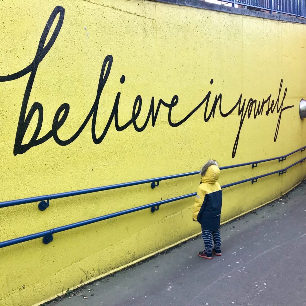 photo of a small child looking at a wall mural that says "believe in yourself" in a post about morning affirmation. 