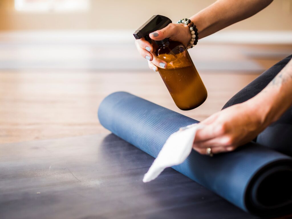 Woman with a cloth, a rolled up yoga mat, and a DIY yoga mat cleaner. 