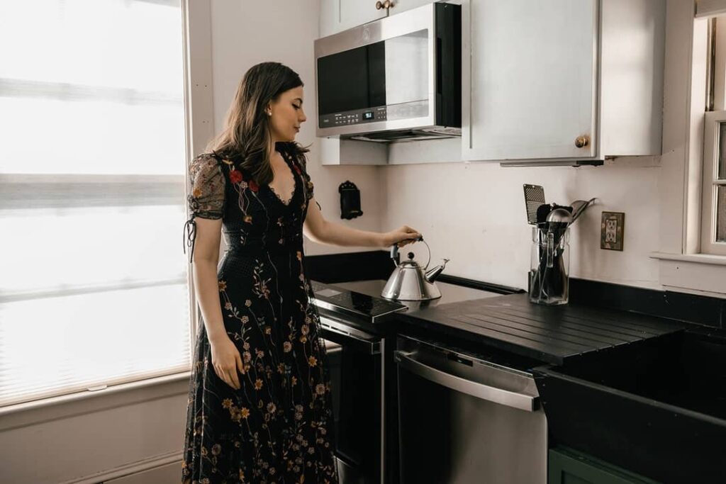A woman standing with a tea kettle on top of the best induction cooktop