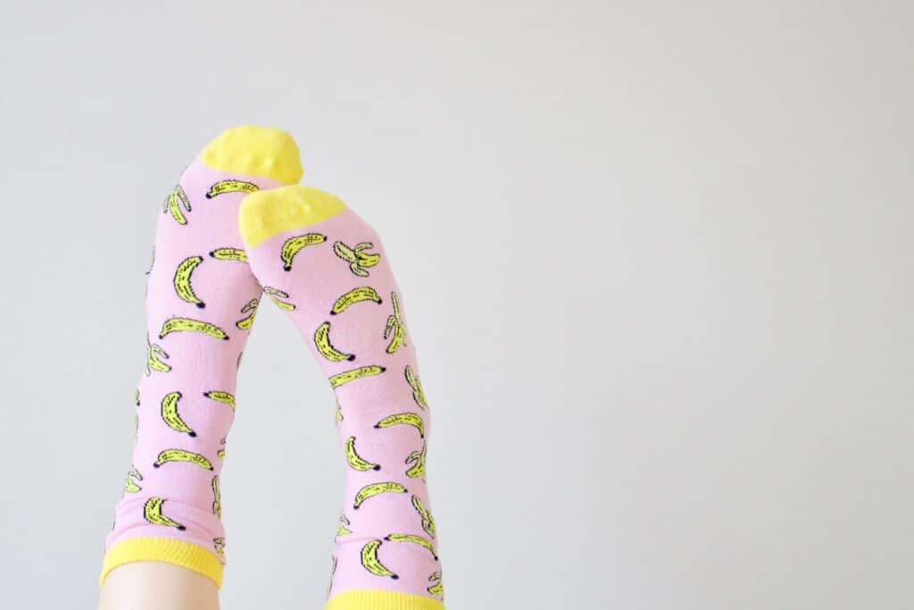 How do you repair a holy sock? Photo of two feet in pink socks with bananas on them in front of a white background. 