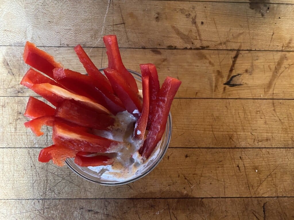 Top view of bell peppers dipped in hummus as a plant based recipe for snacks