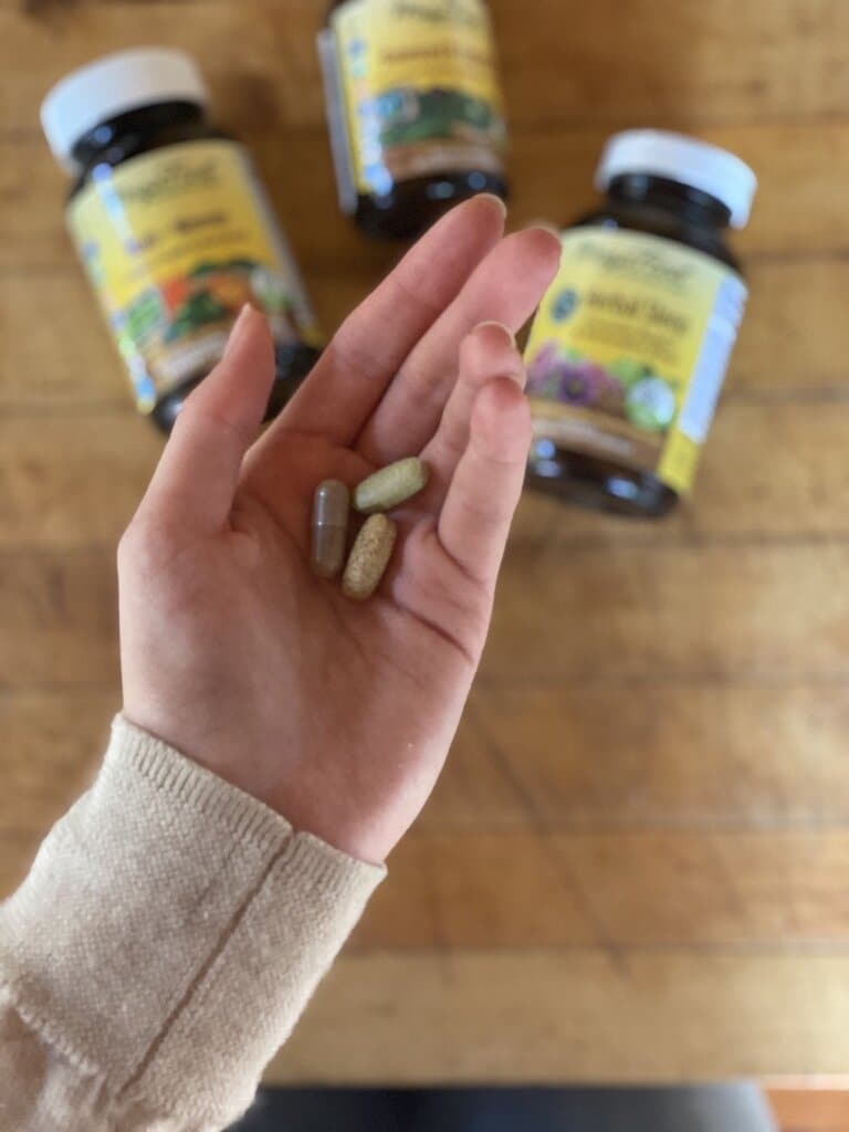 Woman's hand holding 3 supplement/vitamin pills to supplement her whole food plant based recipes