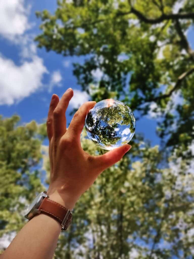 A hand holding a glass orb up to green trees to illustrate the hope we have for a longer Earth over day 