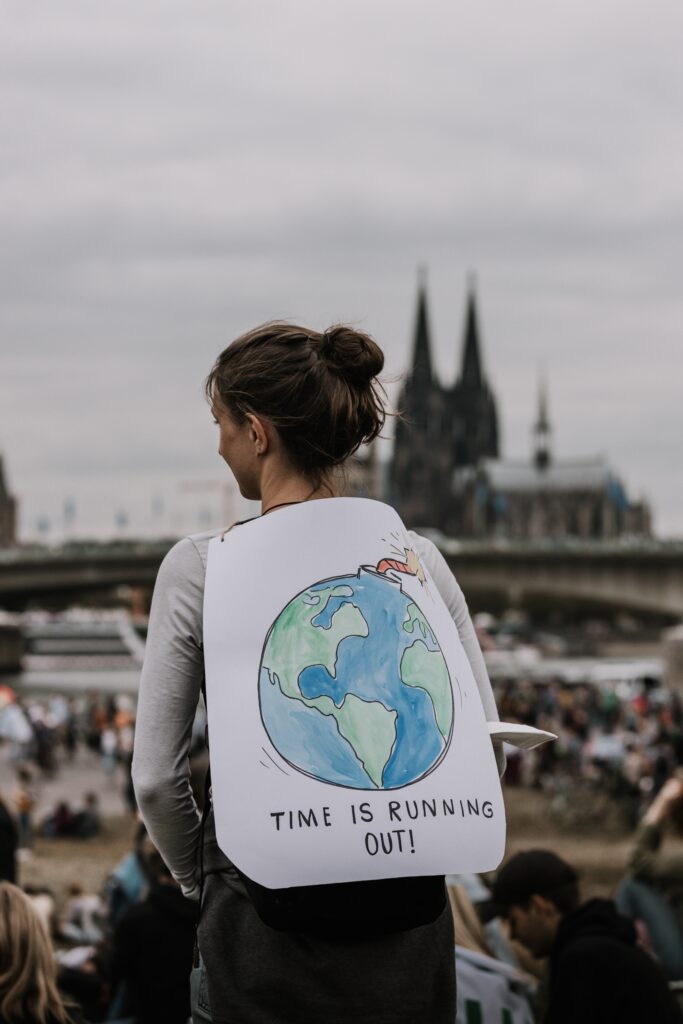 Woman advocating for Earth Overshoot Day at a protest with a sign on her back with Earth shaped as a bomb and text reading "Time is Running out!" 