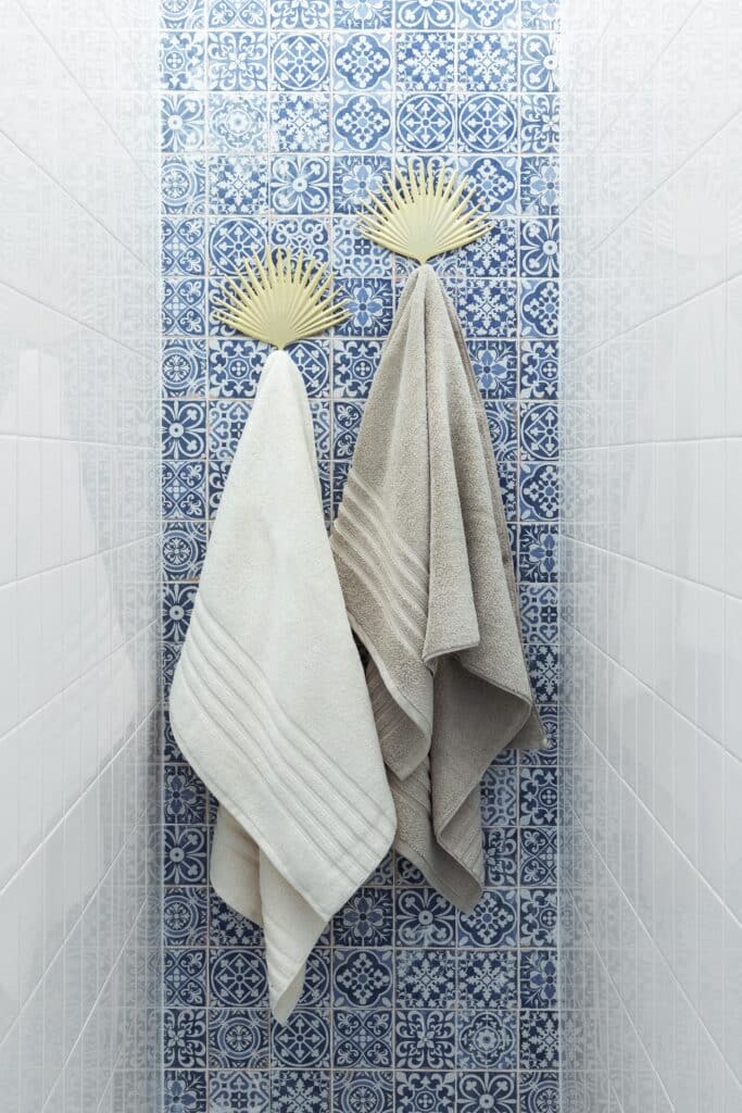 Two eco friendly towels hanging on bath hooks in a tiled room