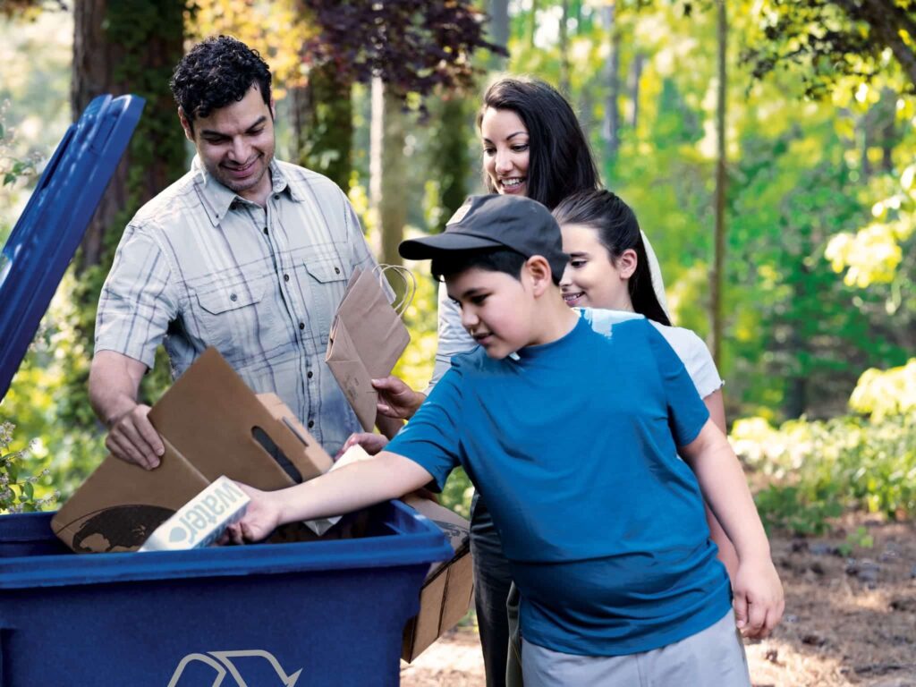 A family placing cardboard and paper bags in the recycle bin in a post about how to recycle paper