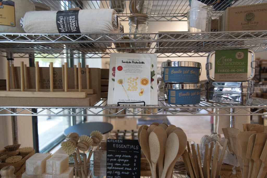 Rack of sustainable shopping items like reusable lunchboxes, wooden kitchen utensils, and unpaper towels. 