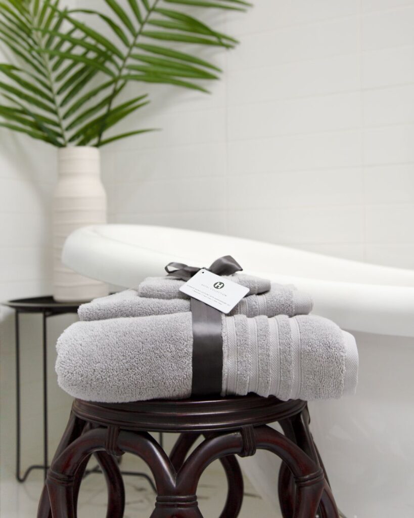 A stack of sustainable towels on a brown stool next to a white tub. 