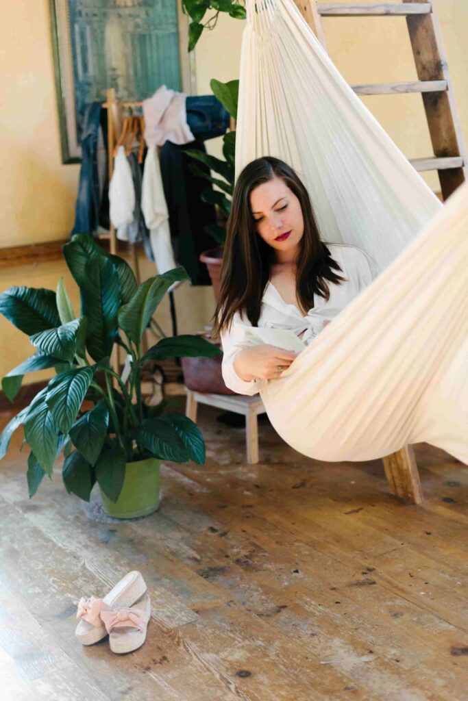 A woman demonstrating how to take care of yourself by reading in her hammock. 