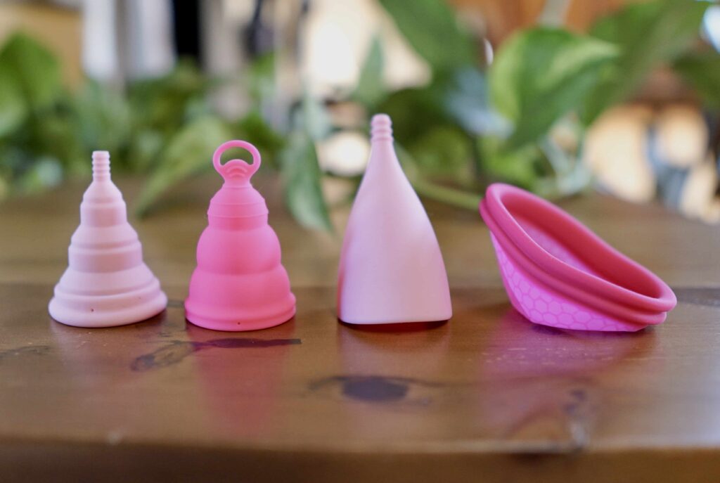 How to use a menstrual cup: various menstrual cups in a row on a wooden table. 