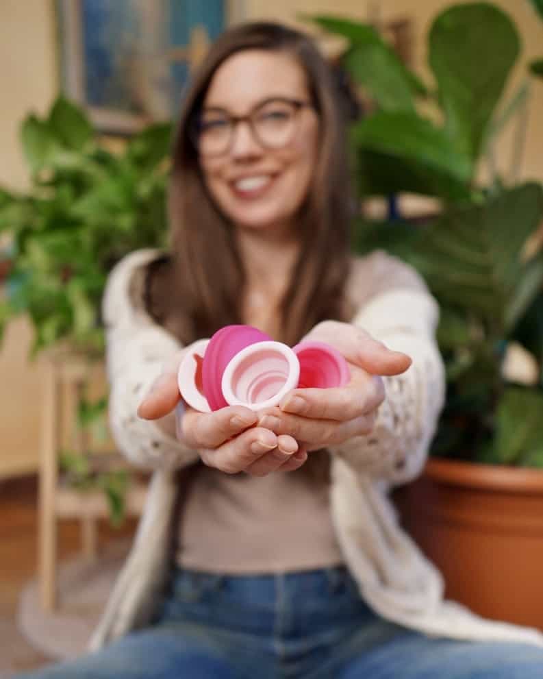 A woman holding a handful of menstrual cups with just her hands in focus. 