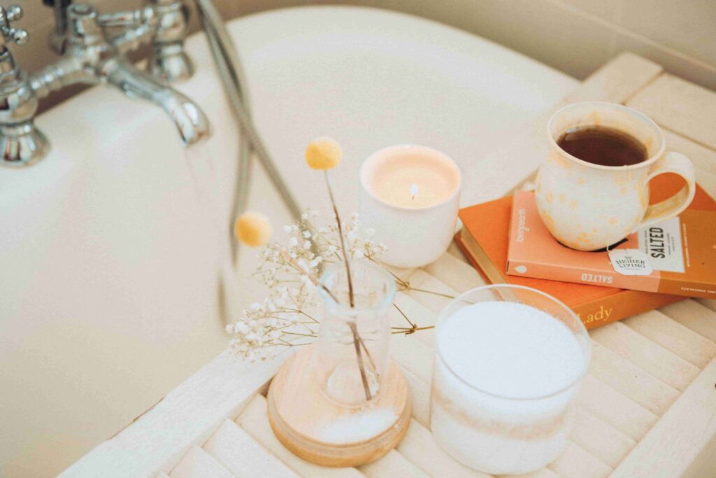 Sustainable self care products: a flower vase, cup of coffee, and candles next to a bath tub. 