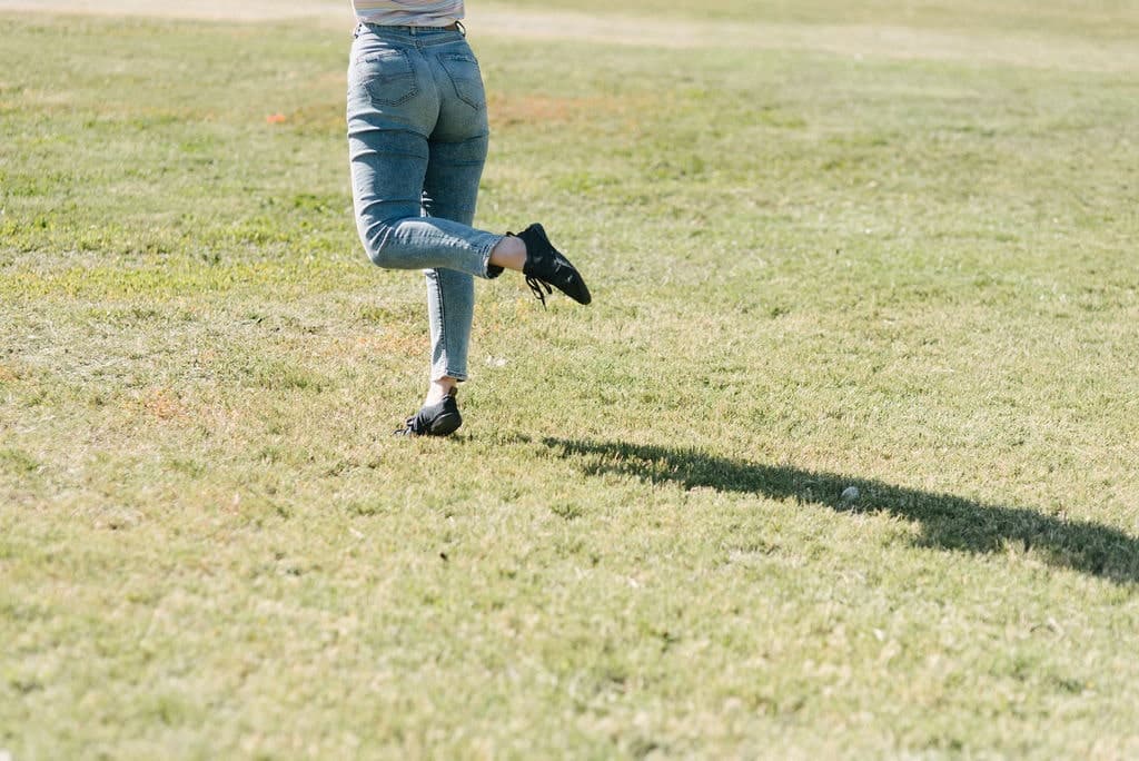 The bottom half of a woman dancing in a pair of Wildlings shoes in an open field.